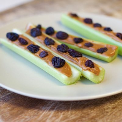 Plate with "ants on a log" which are celery stalks filled with peanut butter topped with raisins.