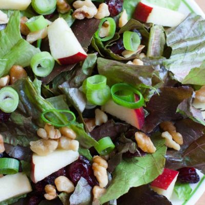 A salad of mixed greens with apples, cranberries, and nuts.