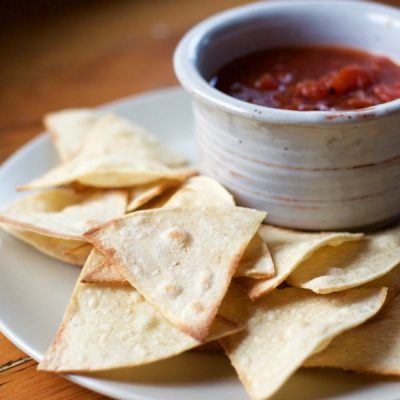 Plate of baked tortilla chips next to bowl of salsa.