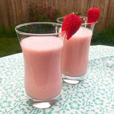 Two glasses of banana pineapple strawberry smoothie with a strawberry on the rim of the glass.