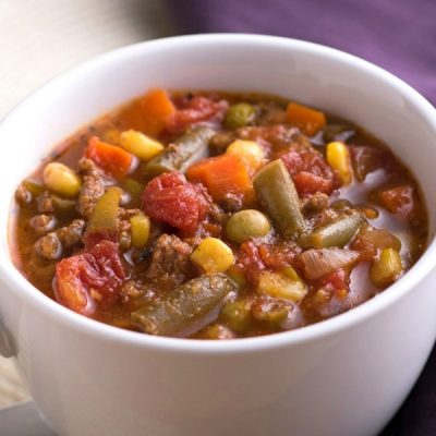 Beef, beans, corn, and other mixed vegetable soup in a small ceramic bowl.