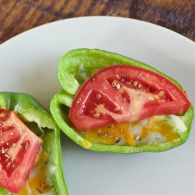 Halved green bell pepper stuffed with shredded cheese and topped with a slice of tomato.