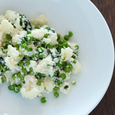 Plate of chopped cauliflower mixed with peas and scallions topped with parsley flakes.