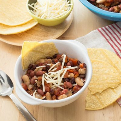 Small bowl of black, great northern, and red kidney beans, mixed with diced tomatoes and topped with grated parmesan cheese.