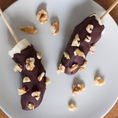 Halved banana placed on popsicle stick and covered with melted chocolate and walnuts.