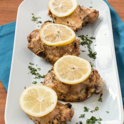 Baked chicken thighs topped with parsley and sliced lemons