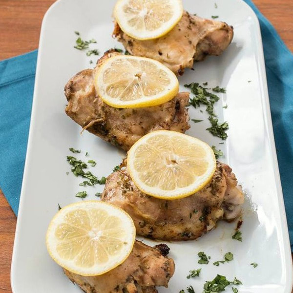 Baked chicken thighs topped with parsley and sliced lemons