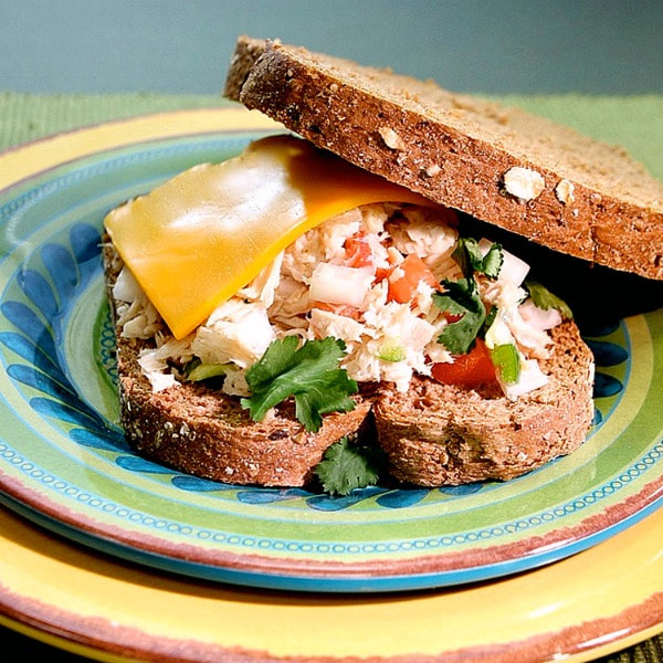 Whole wheat bread sandwich of tuna fish mixed with diced tomatoes, apples, and celery, topped with a slice of American cheese.