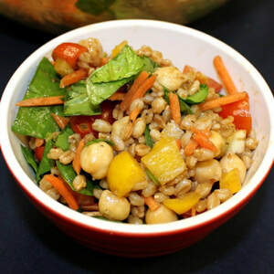 Bowl of boiled farro mixed with chickpeas, halved cherry tomatoes, and diced yellow pepper, carrots, and chopped spinach.