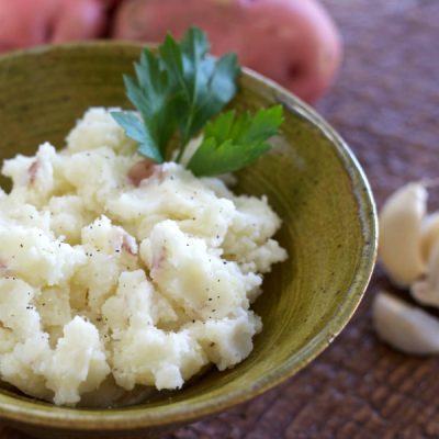 Bowl of creamy mashed potatoes with skins, and topped with a sprig of parsley.