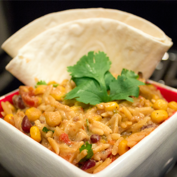 Bowl of cooked brown rice with beans, corn, and diced tomatoes, enchilada sauce, and topped with a sprig of parsley.