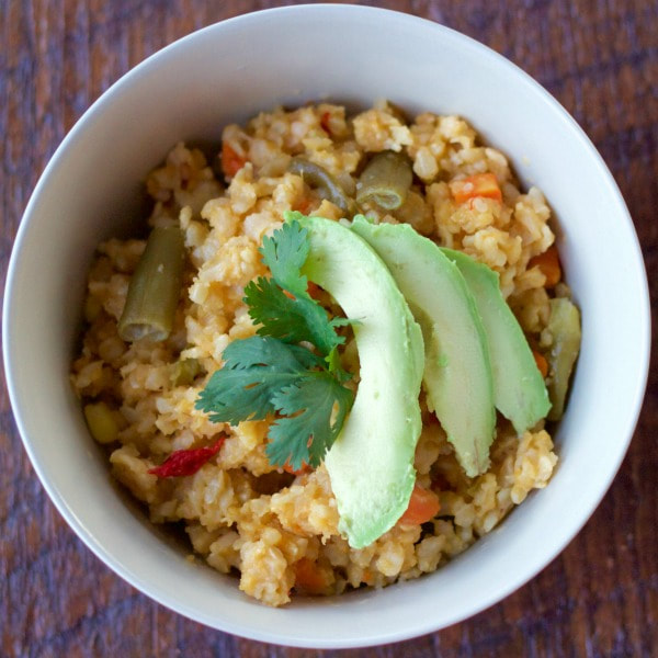 Brown rice topped with garlic, bell peppers, other mixed vegetables, and onions garni9shed with parsley and thin slices of avocado