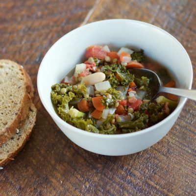 A bowl of kale, onion, garlic, carrot and lentil soup served with a side of bread