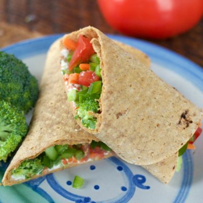 Tortilla wrapped into a burrito stuffed with cream cheese, carrots, onions, tomatoes, broccoli, and bell peppers