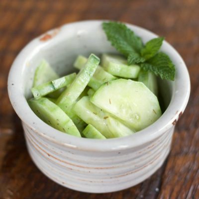 A bowl of cucumber slices mixed with yogurt, dill, and lime juice garnished with mint
