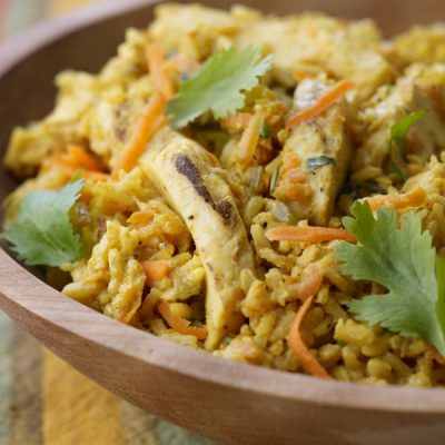 A bowl of curried rice with chicken and vegetables, topped with parsley leaves