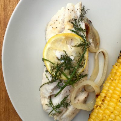 Plate with grilled tilapia topped with lemon and dill, served with corn on the cob
