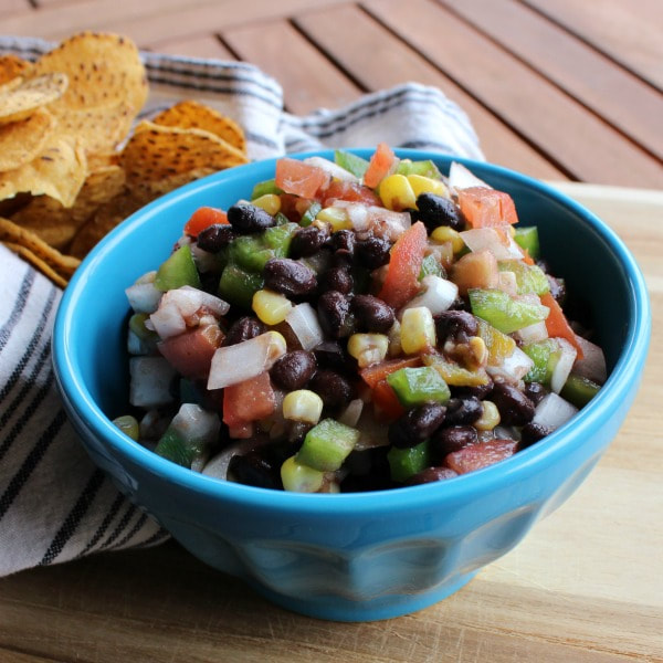 Bowl of salsa made with corn, beans, tomatoes, red onion, green peppers, and garlic, topped with lime juice