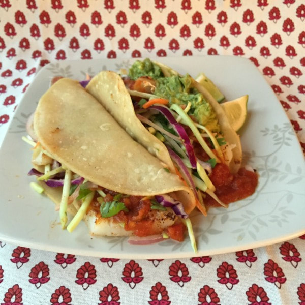 Soft taco shells stuffed with onion, cilantro, coleslaw mic, lime juice, and tilapia, topped with guacamole