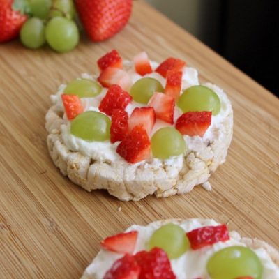 Rice cake topped with yogurt or cream cheese with strawberries and grapes on top.