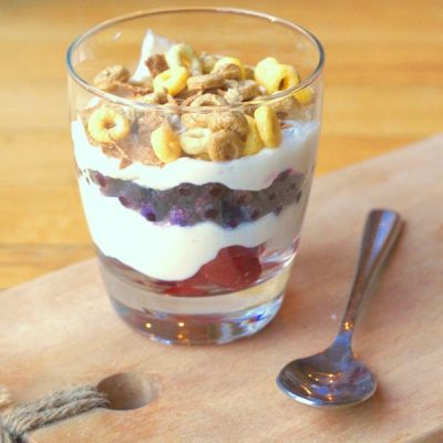 A cup with layers of vanilla Greek yogurt and fruit, topped with crunchy cereal