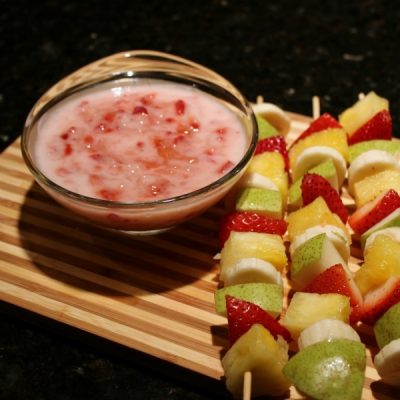 Fruit skewers made of pears, strawberries, bananas, and pineapple served with a side dip of homemade strawberry yogurt