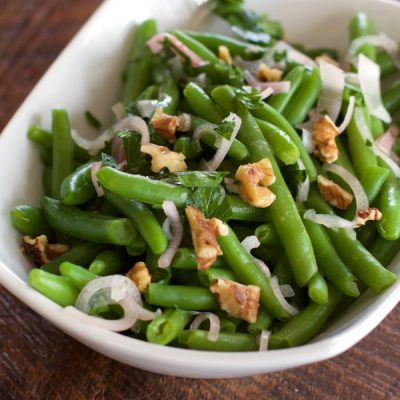 Bowl of green beans with walnuts and onions, garnished with parsley leaves
