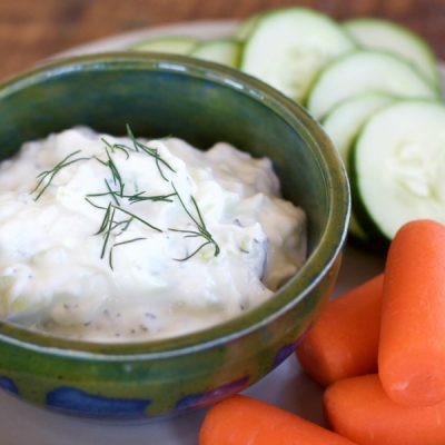 Bowl of Greek cucumber yogurt dip on a plate surrounded by sliced cucumber and carrots