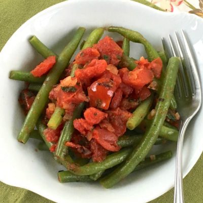 Bowl of cooked green beans topped with a crushed tomato and basil mix with fork