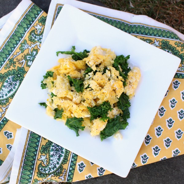 Scrambled eggs with kale, topped with ground pepper on a plate under a patterned cloth napkin.