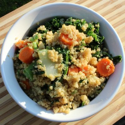 Quinoa and mixed vegetable stir-fry in a white bowl on a wooden cutting board.