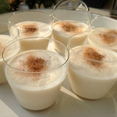Cups of homemade creamy eggnog topped with nutmeg on a serving platter with handles