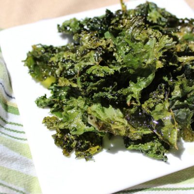 Baked kale chips on a square, white plate resting on a green striped cloth napkin.