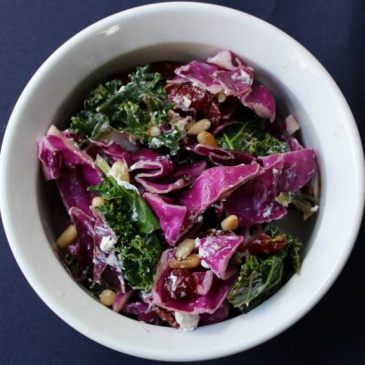 Coleslaw made with kale, red cabbage, crumbled feta, sunflower seeds and dried cranberries in a bowl.