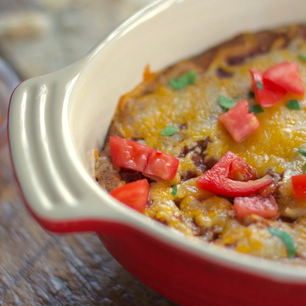 Layered black bean dip topped with cheese, salsa, and cilantro in a red and while oven-dish.