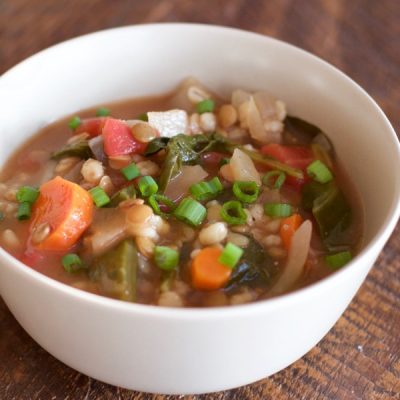 Bowl of lentil, barley, and mixed vegetable soup in a bowl on a rustic wooden table.