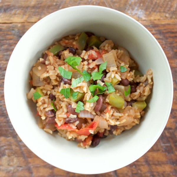 Bowl of meatless dirty rice topped with a green herb on a wooden table.