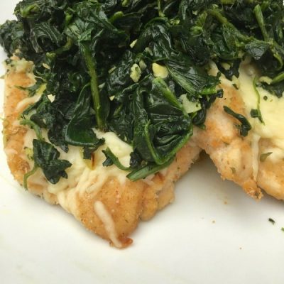 Close up of breaded chicken topped with mozzarella and garlic spinach.