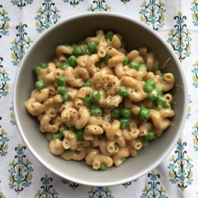 Bowl of mac and cheese with peas topped with ground pepper on a colorful patterned table cloth.