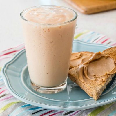Glass filled with papaya banana smoothie with a slice of toast with peanut butter on the side.