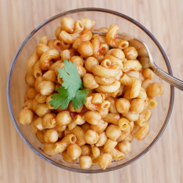 Pasta with chickpeas in a glass bowl with fork. Topped with leaves of parsley on a wooden table.