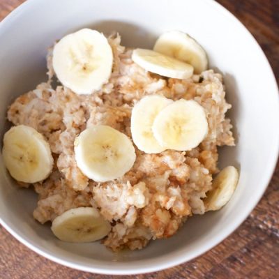 Peanut butter oatmeal topped with banana slices in a bowl sitting on a wooden table.