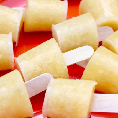 Close up of several mini pineapple orange popsicles with short wooden sticks laying on their sides all on a red plate.