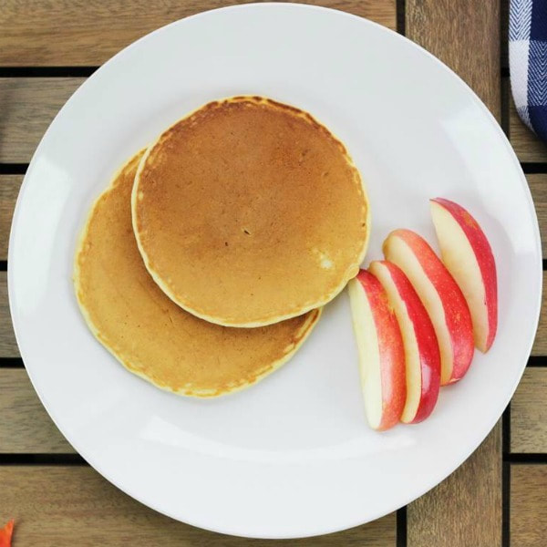 A plate of two overlapping pumpkin pancakes with four apple slices on the side.