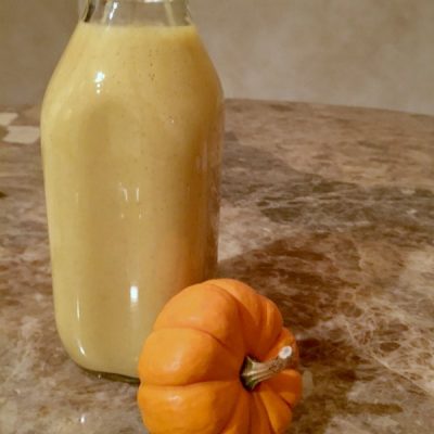 Glass carafe holding a pumpkin smoothie with a small orange gourd next to it.