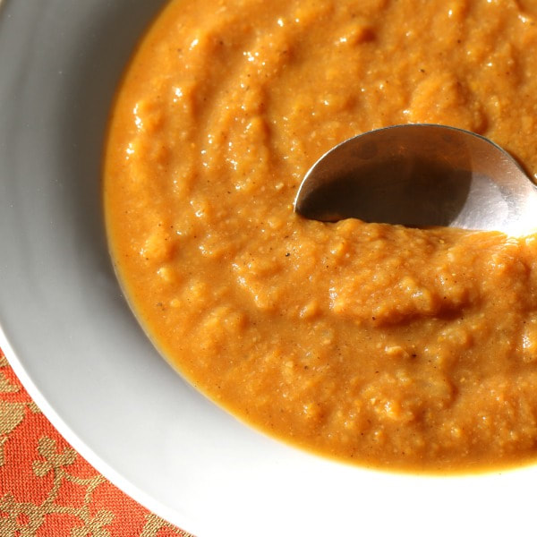 Close up of white bowl holding pumpkin and white bean soup with a spoon in the soup.