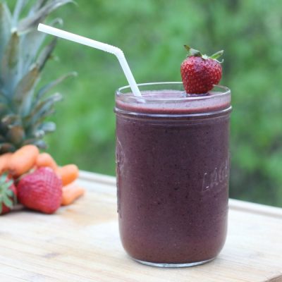 Mason jar with a mixed fruit and vegetable smoothie garnished with a strawberry on the rim with a straw.