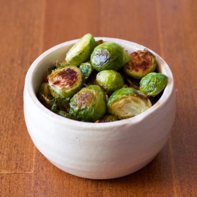 Bowl of roasted Brussels sprouts on a wooden table.