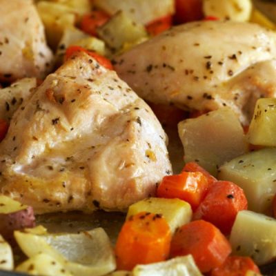 Close up of roasted chicken and root vegetables topped with ground pepper.