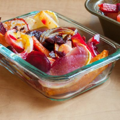 Glass container filled with colorful, roasted root vegetables on a wooden table.